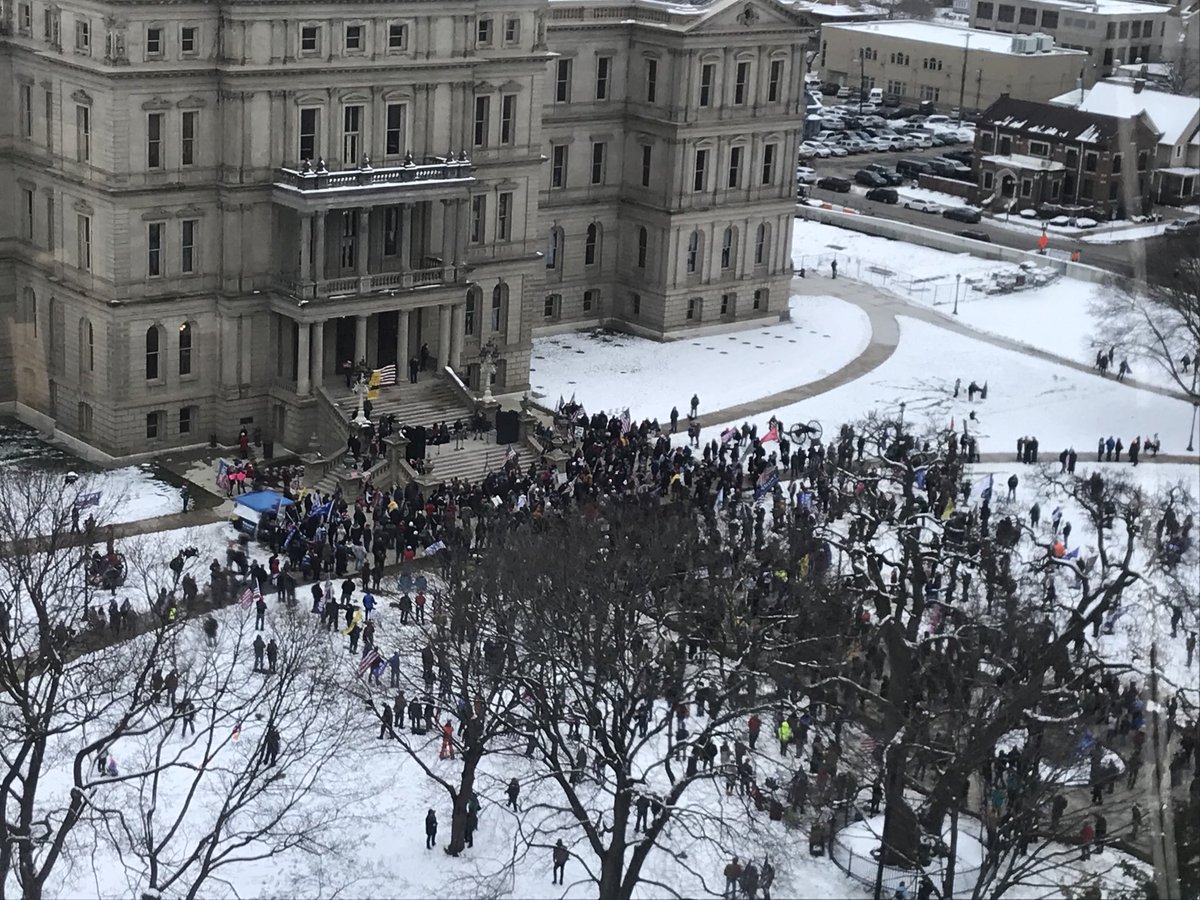 Hundreds of people are standing on Michigan Capitol lawn in the snow, listening to the president's speech over a speaker system